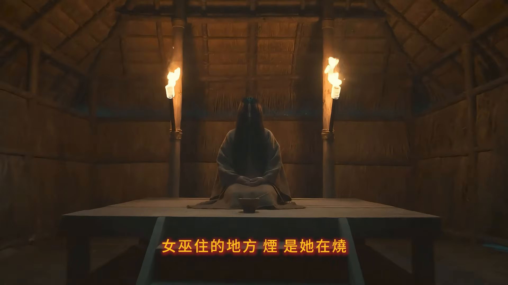 茅屋內垂髮女巫跪坐於木台，兩側火把映出暖光